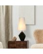 Sfeerfoto van Searchlight Apex tafellamp van 55,5 cm hoog met zwart steenvormige voet en hoge kap van wit textiel op een donker houten kastje naast een wit pluche stoel