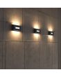 Sfeerfoto van drie Lutec Arteo antraciet grijze rechthoekige wandlampen van 23 cm breed met lichtvenster naar voren, beneden en boven op rij tegen een marmer tegelen muur