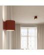 Sfeerfoto van Sollux Aura oker rood geribbeld cilindervormige wandlamp van 10 cm in hoogte met een G9 lampje erin in een woonkamer met een plafondlamp uit dezelfde serie