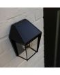 Sfeerfoto met bovenaanzicht van Lutec Avony zwarte wandlamp voor buiten van 20,5 cm hoog met zonnepaneel bovenop en E27 peertje