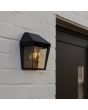 Sfeerfoto met zijaanzicht van Lutec Avony zwarte wandlamp voor buiten van 20,5 cm hoog met zonnepaneel bovenop en E27 peertje