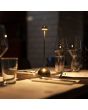 Sfeerfoto van Konstsmide Bandol messing kleurige oplaadbare tafellamp voor buiten van 27 cm hoog met een heel klein metalen kapje op een gedekte dinertafel