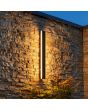 zwarte rechthoekige wandlamp voor buiten met een hoogte van 60 cm en geïntegreerde LED rondom regen een stenen buitenmuur
