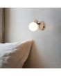 Sfeerfoto van Reality Boba warm beige wandspot van 13,5 cm hoog met rond wit glazen kapje, kiepschakelaar en kabeldoorvoer aan de muur boven een bed