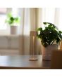 Sfeerfoto van Konstsmide Capri glossy gebroken witte oplaadbare aluminium tafellamp voor buiten van 25 cm hoog met een vierkant kapje met touch dimmer op een salontafel naast een kamerplant