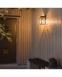 Sfeerfoto van Konstsmide Carpi zwarte wandlamp voor buiten met rechthoekige hangende lantaarn met vier geribbeld glazen ruitjes tegen een houten wand bij een voordeur