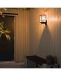 Sfeerfoto van Konstsmide Carpi zwarte wandlamp voor buiten met rechthoekige staande lantaarn met vier geribbeld glazen ruitjes tegen een houten wand bij een voordeur