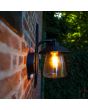 Sfeerfoto van zijaanzicht Lutec Cate antiek bruin zwarte wandlamp voor buiten van 22cm hoog met hangende lantaarn van transparant kegelvormig glas
