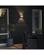 Sfeerfoto van Konstsmide Chieri witte wandlamp van 17 cm breed voor buiten met meerdere lichtpunten met een bijzonder lichteffect op een houten wand in een tuin