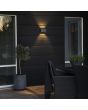 Sfeerfoto van Konstsmide Chieri antraciet grijze wandlamp van 17 cm breed voor buiten met meerdere lichtpunten met een bijzonder lichteffect op een houten wand in een tuin