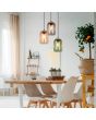 Trio Cork 364630317 sfeerfoto van hanglamp met ronde zwart plafondplaat en drie pendels met amber, groen en rookglazen kappen met bovenzijde van kurk boven een eettafel in een licht interieur