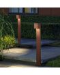 Sfeerfoto van twee Konstsmide Cremona roestbruine aluminium tuinpalen van 100 cm hoog met vierkant kapje met neerwaardse van 0-90 graden instelbare lichtbundel langs een tuinpad