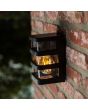Sfeerfoto van bovenaanzicht Lutec Dalton zwarte wandlamp voor buiten van 16,5 cm hoog met transparant kunststof en vier zwart kunststof balken eromheen
