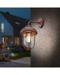 Trio Duero 202760124 sfeerfoto van roestbruine wandlamp voor buiten met hangende kap en transparant glazen bol aan een bruin gestuckte buitenmuur