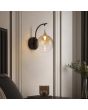 wandlamp met zwarte ophanging van 26cm hoog met hangende kap met goudkleurige bovenzijde en een obre amber kleurige glazen bol met geïntegreerde LED aan een muur