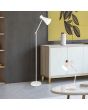 Trio Enzo R50781031 sfeerfoto van mat witte tafellamp met scharnierende arm en metalen spot op een salontafel voor een vloerlamp uit dezelfde serie naast een wit kastje
