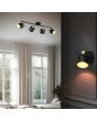 Trio Eva 868800480 sfeerfoto van spot met ronde zwarte plafondplaat en vier spotjes met goudkleurige fitting en zwart kapje met goudkleurige binnenzijde aan twee zwarte stangen boven een cremekleurige slaapkamer met een wandspot uit dezelfde serie