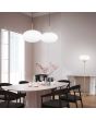 Trio Fomento 363190108 sfeerfoto van twee mat messing hanglampen met 40cm bolvormig wit glas boven een eettafel met een vloerlamp uit dezelfde serie