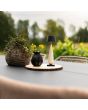 Sfeerfoto van Konstsmide Frejus glossy creme kleurige oplaadbare tafellamp met zwart kapje van 24 cm hoog voor buiten op een tuintafel naast een rieten plantenpot