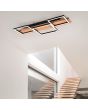 Trio Harper 622910332 sfeerfoto van grote plafondlamp met houten plank en drie zwarte vierkanten met LED strips eronder voor een trapgat naast een raampartij