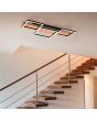 Trio Harper 622910332 sfeerfoto van grote plafondlamp met houten plank en drie zwarte vierkanten met LED strips eronder voor een houten trap
