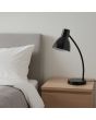 Sfeerfoto van Brilliant Jerry zwart metalen bureaulampje van 42,9 cm hoog met metalen kapje voor een e14 kogellampje op een houten nachtkastje naast een beige bed