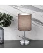 Trio Jerry R50491011 sfeerfoto van tafellampje met chromen lampvoet en grijs cilindervormig lampenkapje van textiel op een grijs blad naast een vaas en voor een marmeren wand