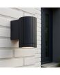 sfeerfoto van een zwart geribbelde wandlamp voor buiten van 10cm hoog met naar beneden gericht gu10 spotje naast een voordeur