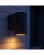 sfeerfoto van een zwart geribbelde wandlamp voor buiten van 10cm hoog met naar beneden gericht gu10 spotje naast een voordeur in het donker