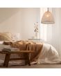 Sfeerfoto van Reality Kibito hanglamp van natuurlijk katoen met een ovale kap met een diameter van 32 cm boven een bed met houten bankje ervoor