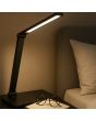 Sfeerfoto van de Brilliant Lomina oplaadbare zwarte bureaulamp van 38 cm hoog met twee scharnierpunten en langwerpige LED unit in de kop op een nachtkastje