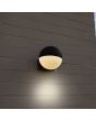 Sfeerfoto van Lutec Looma antraciet grijze wandlamp voor buiten met een bolvormige kap van 15 cm in diameter met wit kunststof onderzijde aan een wit stenen muur