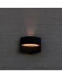 Sfeerfoto met vooraanzicht van de Lutec Lotus zwarte wandlamp voor buiten van 18 cm breed met ovale LED unit naar beneden en een streep licht naar boven