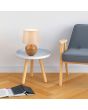 Trio Luxor R50621035 sfeerfoto van tafellampje met bolvormige houten lampvoet en kap van beige textiel op een wit bijzettafeltje naast een houten stoel met blauwe zetel