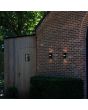 Sfeerfoto van twee Lutec Mika zwarte wandlampen voor buiten van 19 cm hoog met up en down light en LED rand halverwege de lamp tegen een rood ruw stenen muur