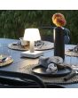 Sfeerfoto van Konstsmide Monaco witte tafellamp van aluminium met wit glazen kapje en touchdimmer van 19 cm hoog op een zwarte gedekte tuintafel