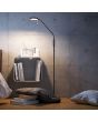 Trio Monza 423310132 sfeerfoto van mat zwarte staande leeslamp met ronde kop met LED paneel en dimmer op de paal naast wat boeken en kussens