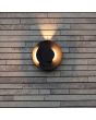 Sfeerfoto van Lutec Moov antraciet grijs schijfvormige wandlamp voor buiten met een diameter van 21,1 cm met lichtbundel naar boven en twee draaibare schijven met richtbare LED bundels