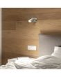 Sfeerfoto van Reality Nancy staalkleurig wandspotje van 9,5 cm hoog met GU10 lamp, kiepschakelaar en mogelijkheid voor kabeldoorvoer naast een grijs bed aan een houten wand