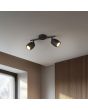 Sfeerfoto van Reality Nancy zwarte plafondspot van 27,5 cm lang met twee metalen spotjes met GU10 lamp aan een plafond voor een raam en een wand met houten latjes