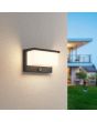Trio Nestos 240969142 sfeerfoto van antraciet grijze wandlamp voor buiten met witte rechthoekige lichtunit en bewegingsmelder aan een spachtelputz muur met zichtbaar lichtbeeld