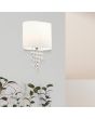 Searchlight Nina 1051-1CC sfeerfoto van wandlamp met ovale kap van textiel en vijf kettingen eronder van kristallen aan een muur boven een kamerplant