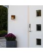Sfeerfoto van Konstsmide Pistoia roestbruine wandlamp voor buiten van 17,5 cm hoog met een buisvormig kapje met streepvormige openingen voor het licht naast een voordeur
