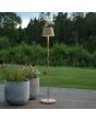 Sfeerfoto van Konstsmide Pomezia zandkleurige aluminium IP54 terraslamp van 124 cm hoog met rond kapje naast twee plantenpotten voor een vergezicht