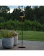 Sfeerfoto van Konstsmide Pomezia mat zwarte aluminium IP54 terraslamp van 124 cm hoog met rond kapje naast twee plantenpotten voor een vergezicht