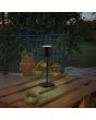 Trio Fernandez R54096132 sfeerfoto van zwarte oplaadbare tafellamp voor buiten op een tuintafel van pallethout op een terras met uitzicht op een boomgaard