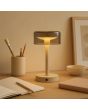 Sfeerfoto van de Brilliant Razor beige oplaadbare tafellamp van 26 cm hoog met rond rookglazen kap van 12 cm in diameter op een houten tekentafel