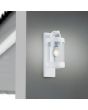 Trio Sambesi 204160131 sfeerfoto van witte wandlamp voor buiten met een rechthoekige wandplaat en hangende cilindervormige kap met dag nacht sensor aan een gestucte muur