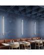 Sfeerfoto van drie smalle beige wandlampen Sappo van 120 cm lang met LED voor indirect licht langs een blauwe muur in een restaurant