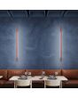 Sfeerfoto van twee smalle okerrode wandlampen Sappo van 120 cm lang met LED voor indirect licht boven een bank voor een eettafel in een restaurant